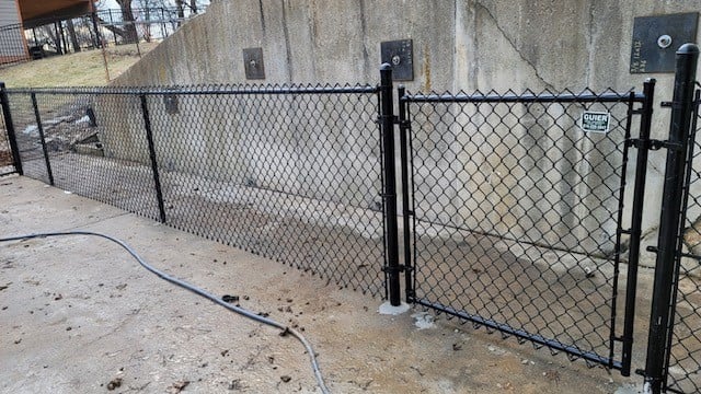 Black chain-link fence gate against a concrete wall.