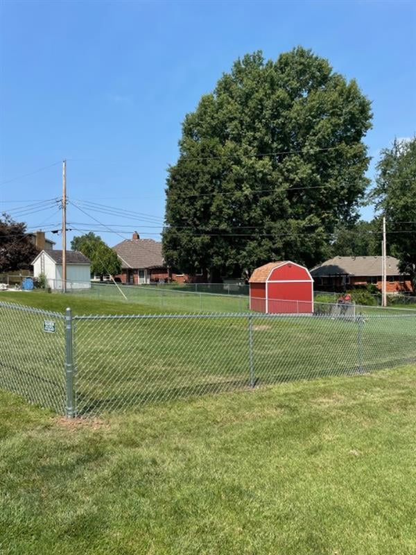 A fenced backyard with green grass and a red garden shed under a clear blue sky.