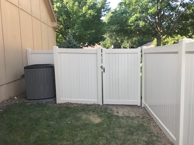 White vinyl fence gate with greenery behind it.
