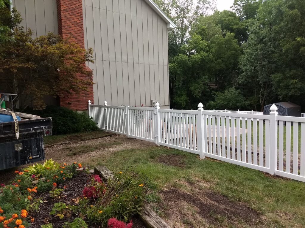 White picket fence separating garden from yard near a house.