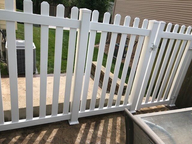 White vinyl picket fence gate with latch, on a sunny day.