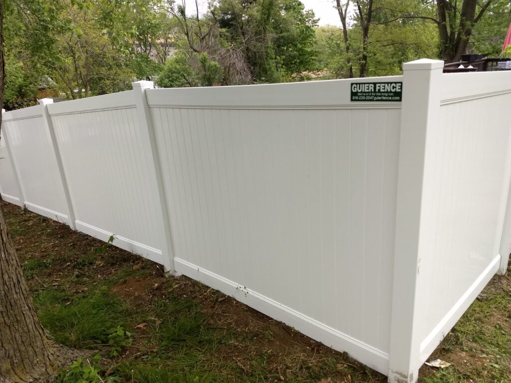 White privacy fence with a small green sign in a backyard.