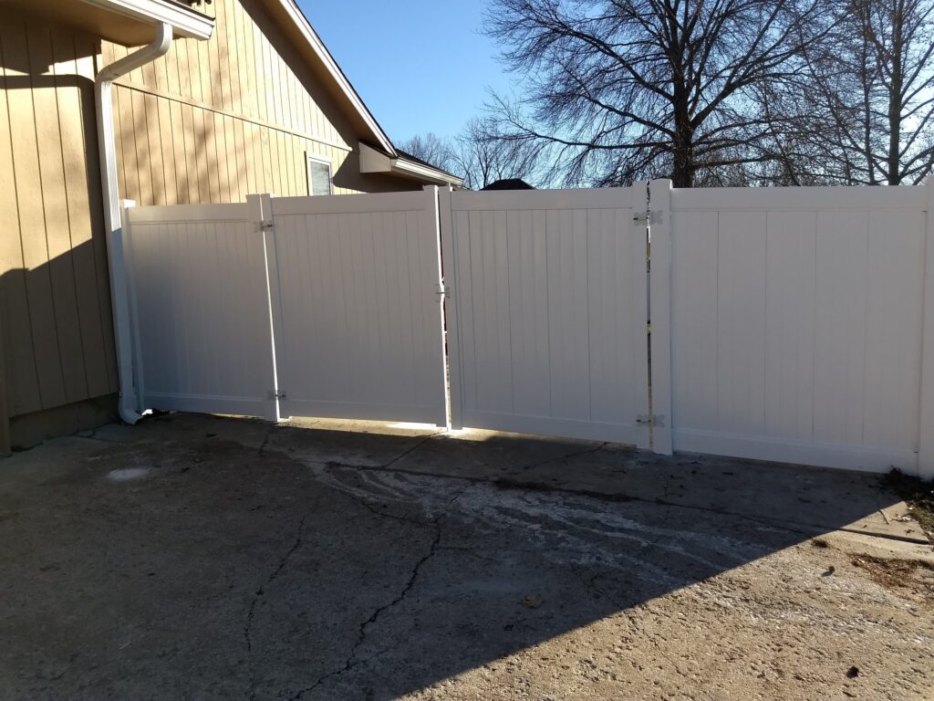 White vinyl privacy fence with gate in a sunny backyard.