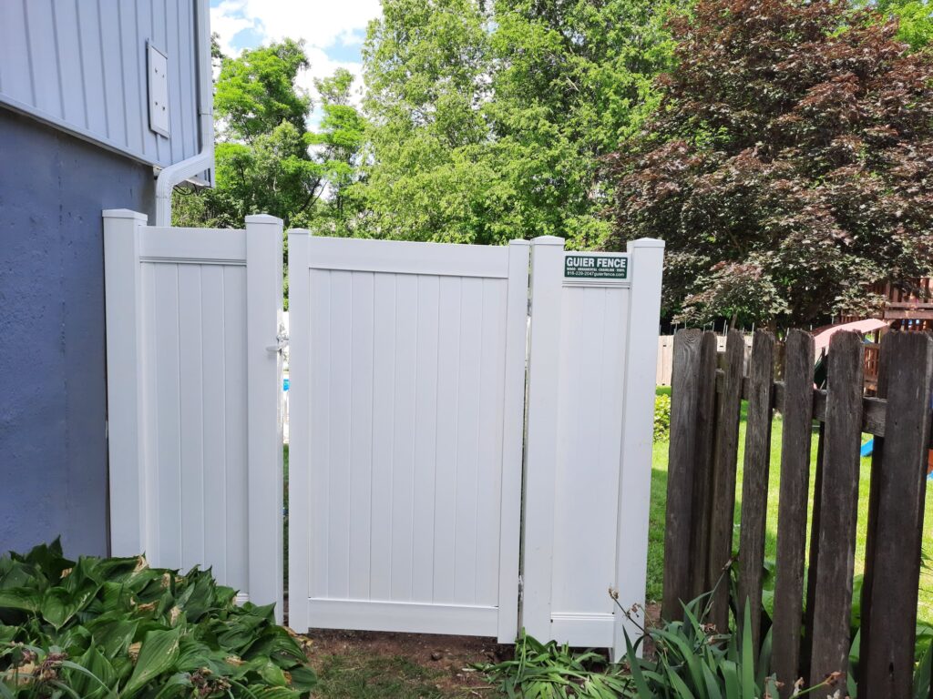 White wooden gate with greenery behind it in a backyard.