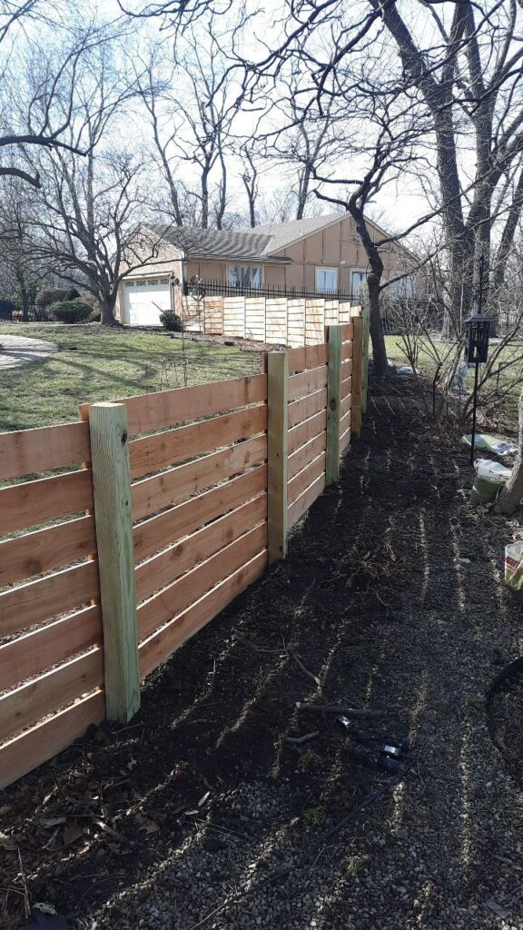 A newly installed wooden fence with horizontal slats in a backyard.
