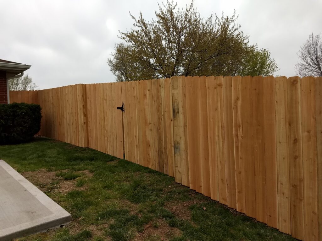 New wooden fence with a closed gate and tree in the background.