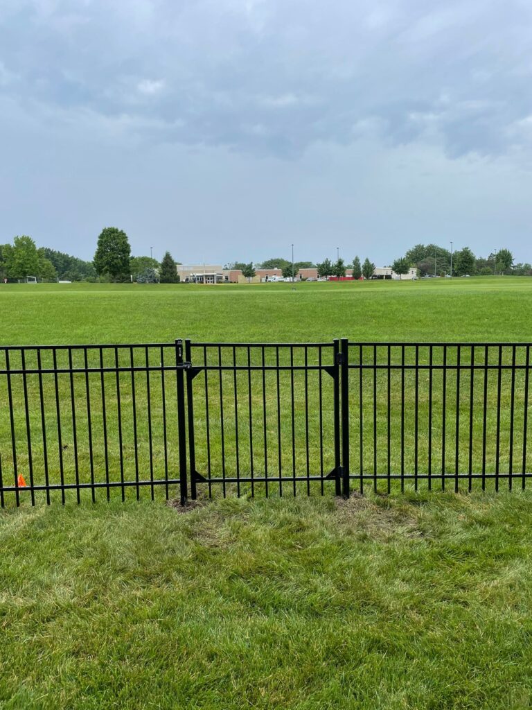 A black metal fence bordering a green field under a cloudy sky.